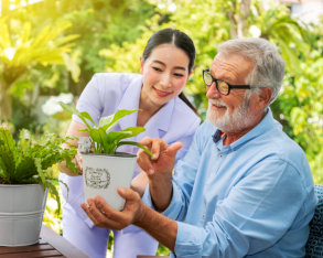 caregiver showing pot of plant to elderly man