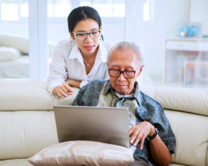 caregiver assisting an elderly man use a laptop